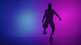 Black man a player juggles football ball in a dark studio with neon lights on the floor and red and blue lighting effects in slow motion. African professional football soccer player - Powered by Shutterstock - Get 15% off with code: PIKWIZARD15