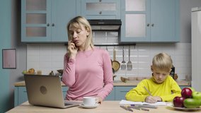 Woman works on laptop, talking on phone, boy draws with felt tip in album. Mom and son in kitchen. Family bloggers filming stories for social media and life video blog. Slow motion ready, 59.97fps.