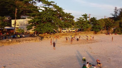 Phuket, Thailand, 11, January, 2022:
A group of people playing volleyball on the court on the beach at sunset, aerial view