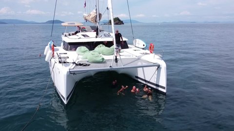 Phuket, Thailand, 20, December, 2019:
A group of tourists bathe under the net of a sailing catamaran, a group of tourists hid from the sun in the water under the catamaran