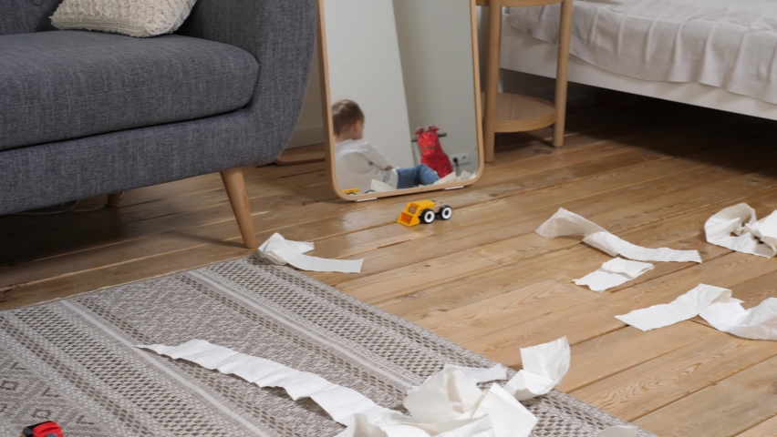 Small child has made a mess, scattered toilet paper around the apartment and happily plays. Little child having fun in the midst of chaos Royalty-Free Stock Footage #1086445475