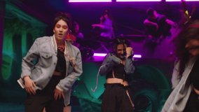 Group of stylish young people dancing , moving near military tank inside garage building Colorful stylish clothes , hippie style fashion . Modern professional dances . Purple led light , slow motion