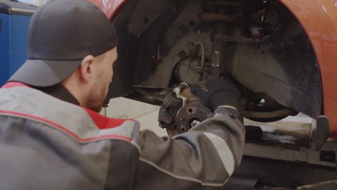 Mechanic in uniform turning wheel disc while repairing car in service garage