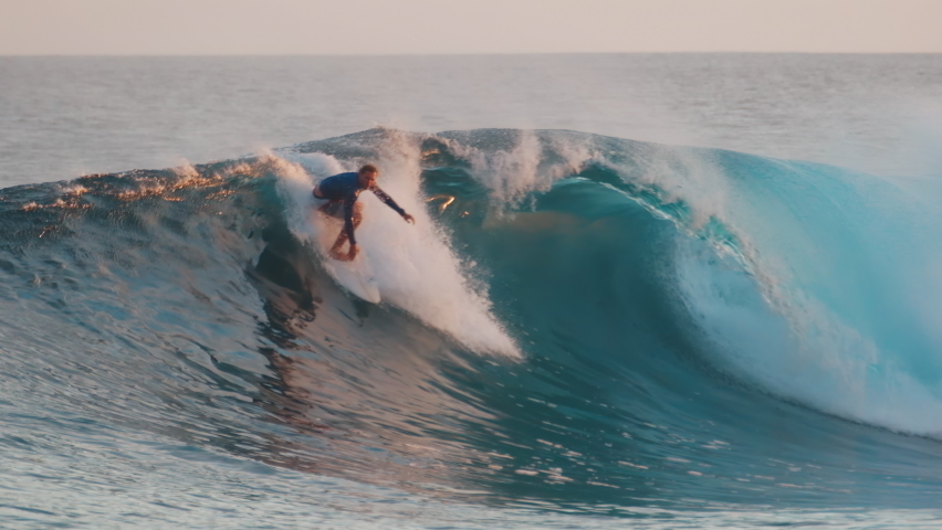 Surfer rides big wave in Maldives during sunset