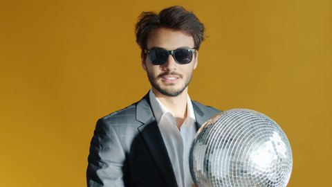 Slow motion portrait of joyful Middle Eastern man holding mirrorball and smiling looking at camera while glitter lights illuminating face