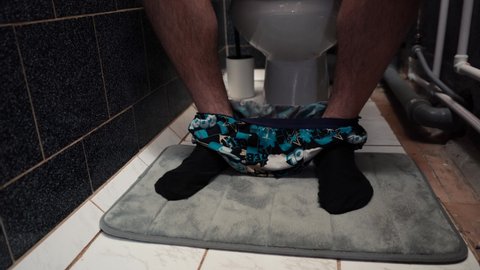 man sits on the toilet taking off his underpants