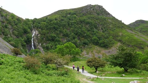 Distant rear view of group of three people walking on footpath to waterfall in Snowdonia National Park, Wales, United Kingdom.
