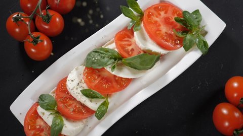 Falling pepper over tomato mozzarella salad. Top view. Slow moion. caprese salad with ripe tomatoes and mozzarella cheese with fresh green purple basil leaves. Healthy food and vegetarian concept