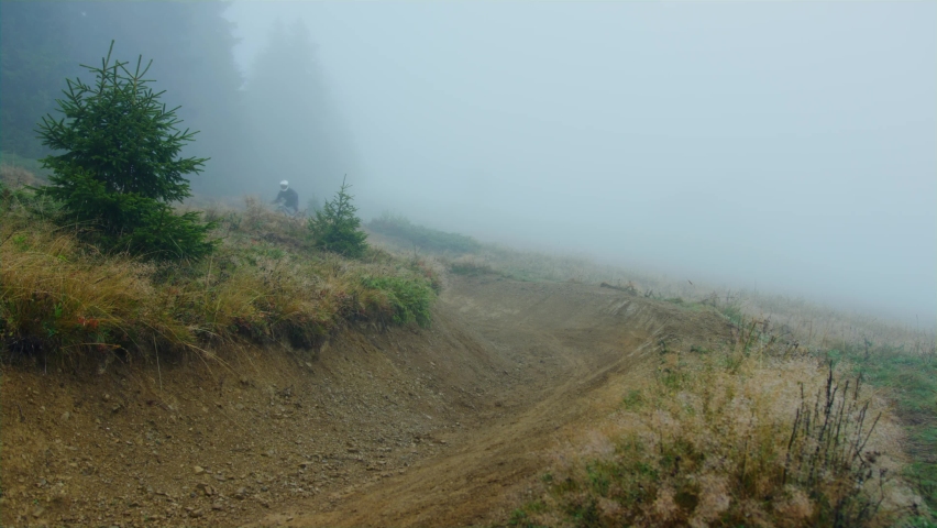 A mountain biker rides an alpine trail covered in fog