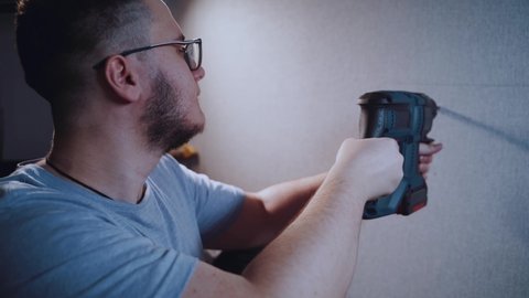 A man drills a wall with a hammer drill in his apartment