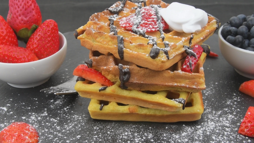 Belgian waffles for breakfast or brunch with fresh blueberries, strawberries, melted chocolate and whipped cream on top. Rotating stack of waffles | Shutterstock HD Video #1086479465