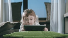 Small Child Hold Pad Computer Surfing Internet Play Game At Home Alone. Preschooler Girl Lying On Sofa Surfing Internet Watching Video Internet Education Concept