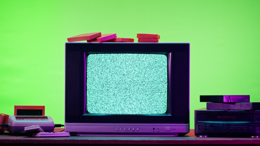 Old television with grey interference screen on purple neon background. Close-up of vintage tv and cartridges for retro playstation. Antique video game, nostalgia.  | Shutterstock HD Video #1086482318