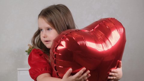 little cute girl in a red dress gently hugs red heart shaped balloons with her hands. valentines day concept