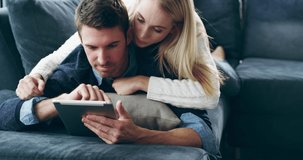 Once again, technology brings people closer. 4K video footage of a young woman being affectionate with her husband while he uses a digital tablet at home.