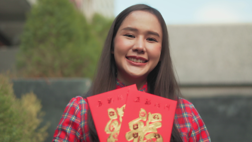 Beautiful Asian woman wearing a traditional red cheongsam on Chinese New Year.Hand holding red envelope or Ang pao with Chinese character means happiness or good fortune.