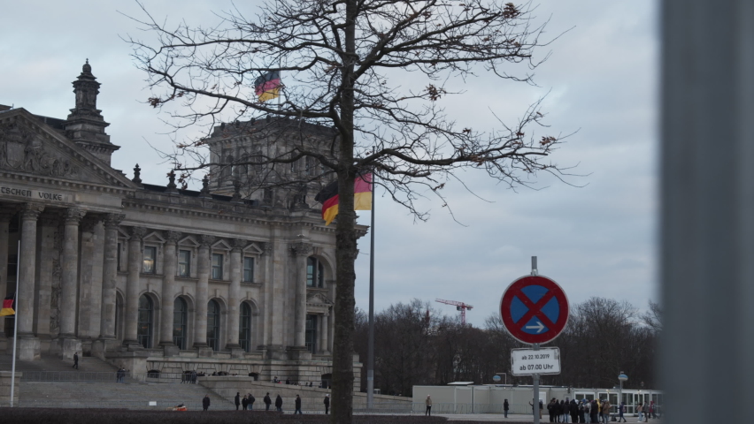 View of historic building on German parliament. Tourists in front of Deutscher Bundestag. Flags waving on poles. Berlin, Germany