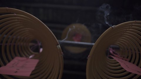 Hong Kong spiral incense sticks with tied pink papers hang in ancient Buddhist temple low angle shot. Traditional ritual to attract good luck