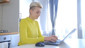 Tomboy woman working on computer. Beautiful young female with dyed short hair typing on laptop keyboard at home during lockdown. Freelancer person using notebook for distant work online