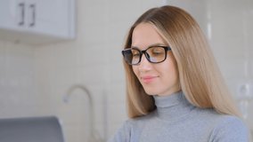 Beautiful blonde woman in glasses working on laptop at home. Portrait of attractive young female doing distant work online during lockdown. Focused freelancer person using computer in 4k video