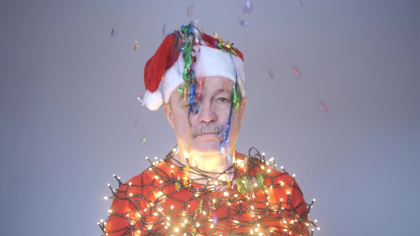 Senior sad man in red christmas hat wrapped in garland.