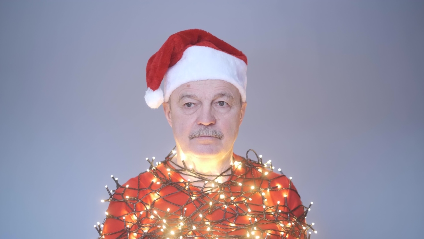 Senior sad man in red christmas hat wrapped in garland.