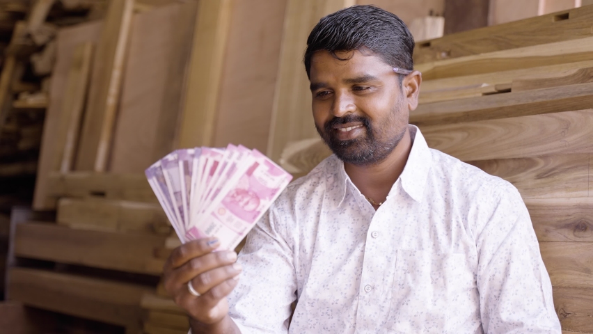 Happy young indian carpenter holding money or Indian currency notes by loooking at camera - concept of professional occupation, earnings, profits in business and finance.