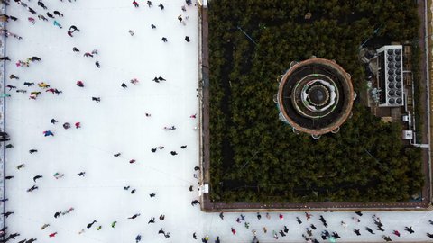 Aerial Drone View Flight Over many people in colorful clothes skating on open-air ice rink in winter. Urban Ice skating top view. City Park, Public Ice Rink. Winter outdoor. Skating sport background