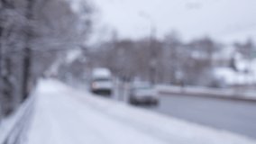 Snowy blured urban road and traffic. 4k stock video footage of blurry city street, white sidewalks covered with fresh snow, cars driving