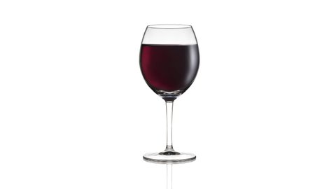 Empty wineglass filling up with red wine on white background