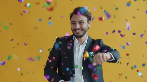 Slow motion portrait of excited dancing enjoying confetti at party on yellow color background. Celebration and decor concept.