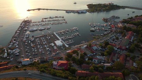 Aerial of seaside town, Sozopol. Huge port surrounded by many boats. Bunch of vehicles parked nearby the port. Drone view of a summer sunset 