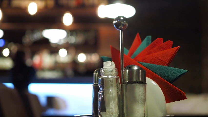a stand with napkins on the table in a cafe with a blurred bokeh. the people in the background at the bar are blurry bokeh. unrecognizable silhouettes of people in the background