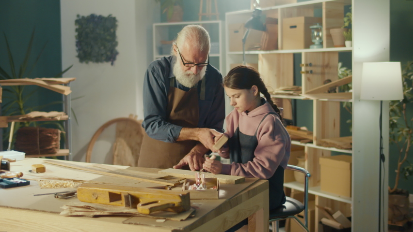 Grandfather Carpenter with Granddaughter Work with Wood to Create Items or Furniture Using Carpentry Tools. Training in Craft Skills in Home Workshop. Communication of Generations. Handicraft, Hobby.