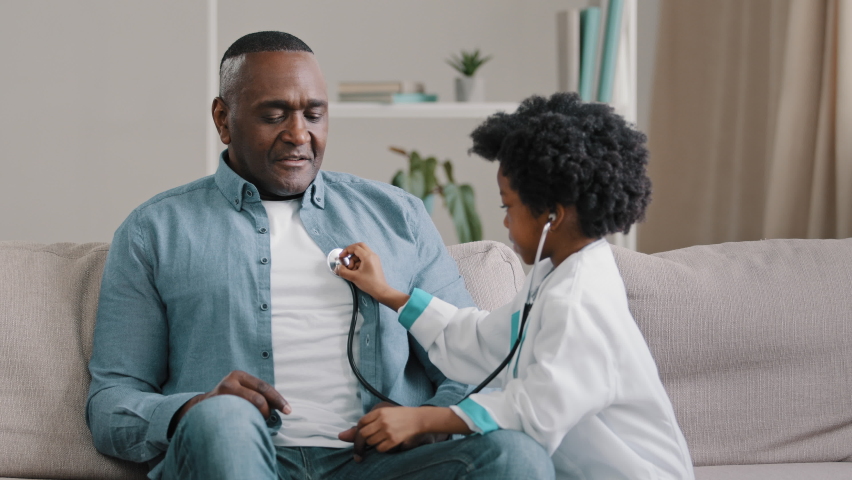 Little african american girl in medical gown plays sitting on couch kid doctor listens to father stethoscope pretends nurse having fun loving daughter forbids dad to smoke indicates get rid bad habit Royalty-Free Stock Footage #1086510095