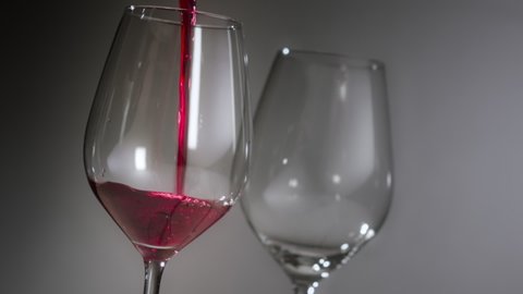 Red wine is poured and fills a wine glass almost to the top, suggestive of drinking too much or alcohol addiction. Filmed against neutral background.