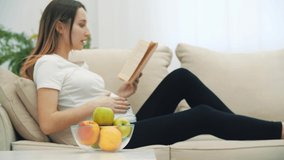 4k video of pregnant woman reading a book and eating an apple.
