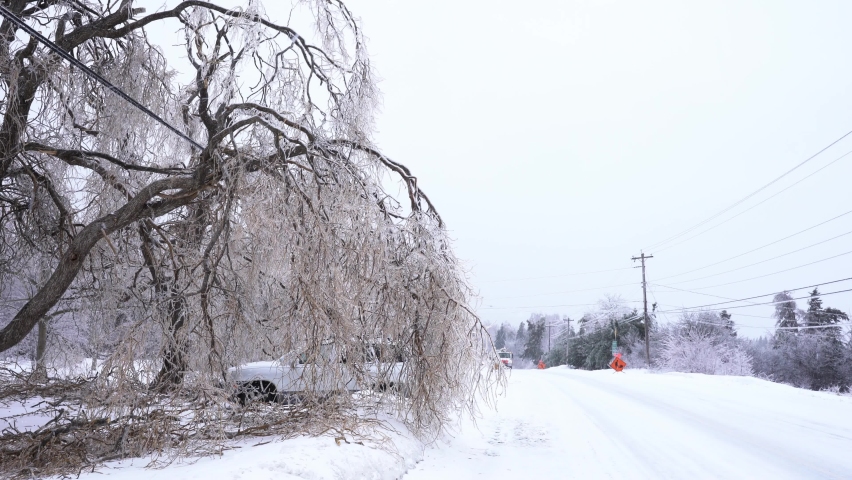 A major ice storm causing electrical power outages.  Ice covered trees hanging over power lines while repair crews head to work on the power lines using aerial lift bucket trucks Royalty-Free Stock Footage #1086517439