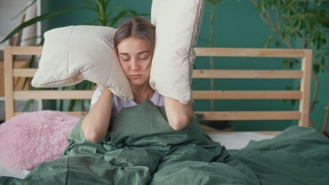 A Young Woman in Bed Tries To Rest, Irritated By Noisy Neighbors. Insomnia, Thin Walls of the House, Apartment Without Sound Insulation, Repair Work at the Neighbors. The Concept of Neighborhood.