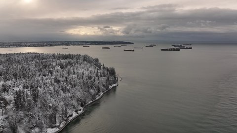 Vancouver, British Columbia, Canada - Aerial view of Stanley Park and the Pacific Ocean with cargo ships on a Snowy Winter day in 4K