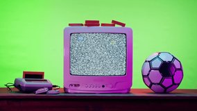Old television with grey interference screen on green neon background. Close-up of vintage tv and cartridges for retro playstation. Antique video game, and football ball, nostalgia. 