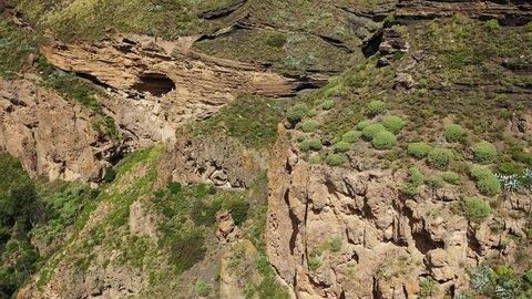 Birds eye view over spectacular rock formations on the edge of a volcano crater in Gran Canaria of Canary islands against the backdrop of lush green valleys.