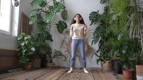 Positive young italian woman in wireless headphones listening to music with pleasure, enjoying the moment, relaxing, dancing on wooden floor in cozy home garden with monstera and tropical plants.  - Powered by Shutterstock - Get 15% off with code: PIKWIZARD15