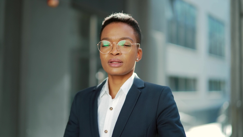 portrait of confident serious african american business woman standing with arms crossed looking at camera. outdoors. Independent female teacher or associate professor with glasses on the outside Royalty-Free Stock Footage #1086545597