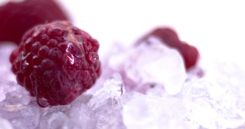 Raspberries on cold ice. A drop of water falls on the raspberry. Natural cold fruits, juicy and aromatic food.  Slow motion, 8K downscale. 4K.