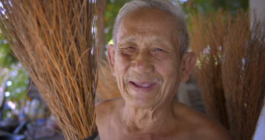 Smiling Asian male farmer who is an elderly person makes brooms from the grass that has many names called Paddy's lucerne, Queensland hemp , Arrowleaf sida , Common sida , Cuba juite for extra income. Royalty-Free Stock Footage #1086552218