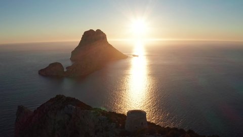 Aerial view of sunset behind Es Vedra Ibiza with pirate tower in the foreground. Showing ocean and clear skies.