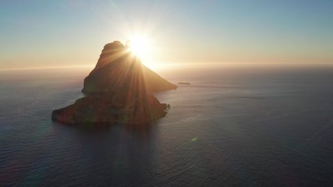 Aerial view of sun coming from behind Es Vedra Ibiza. Showing ocean and clear skies.
