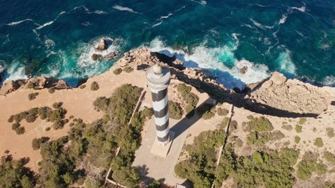 Aerial view dolly in on Punta Moscarter lighthouse in Ibiza, Spain. Showing the lighthouse close up and showing clear ocean and skies, rough waves pounding on the cliffs.