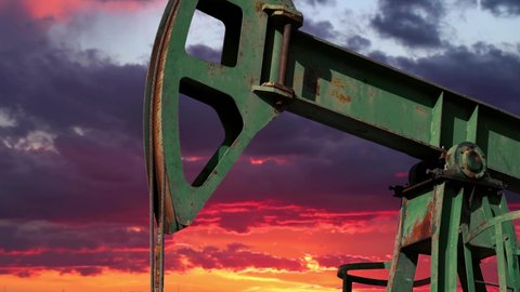 Oil Pumpjack Working Under A Dramatic Sky With Setting Sun. Fossil Fuel Energy. Oil Industry Equipment. Oil Drilling Rig Against Orange Sunset Sky With Moving Clouds.